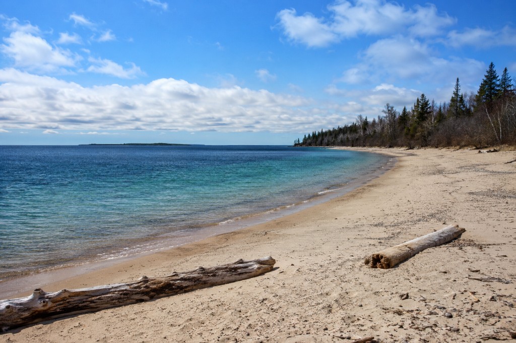 A wide empty sand beach on Lake Superior near Wawa with driftwood and turquoise shallows